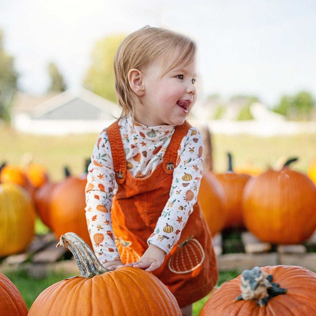 child in orange at a pumpkin patch smiling and having fun